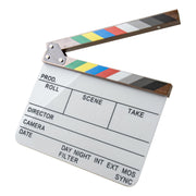 A professional film clapperboard with a white writing surface, black text fields, and a striped hinged top featuring a rainbow of color blocks (green, yellow, red, blue, white, gray, black) and a brown wood-grain finish, isolated on a white background.