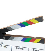 A close-up of a film clapperboard with black and white striped wings, a natural wood edge, and a colorful stripe sequence in blue, green, red, and yellow on the open blade. Part of the white writing surface is visible below, along with cropped text fields for roll, scene, and take.